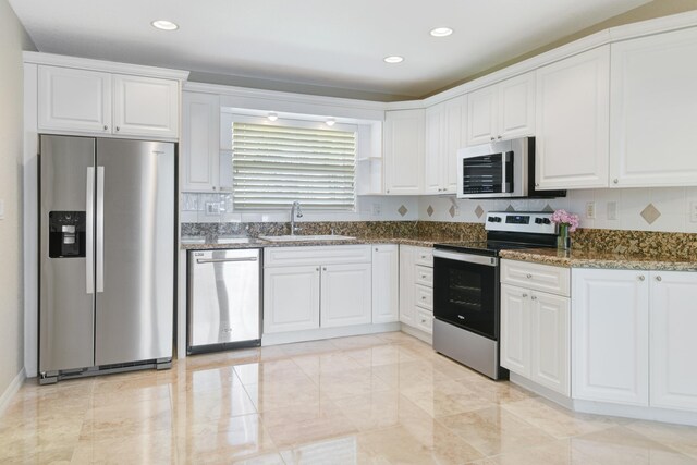 kitchen with white cabinets, appliances with stainless steel finishes, dark stone countertops, and sink