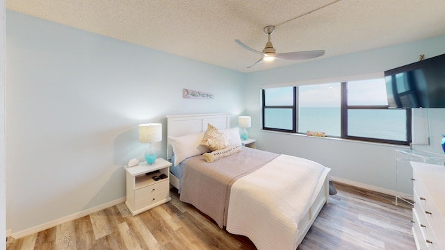 bedroom featuring ceiling fan, light hardwood / wood-style floors, and a textured ceiling