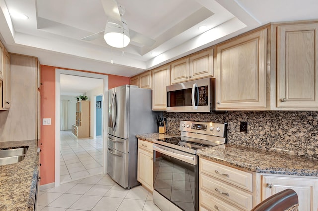 kitchen with ceiling fan, a tray ceiling, stainless steel appliances, backsplash, and light tile floors