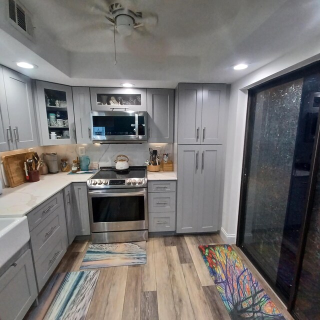 kitchen featuring gray cabinets, appliances with stainless steel finishes, ornamental molding, kitchen peninsula, and light wood-type flooring