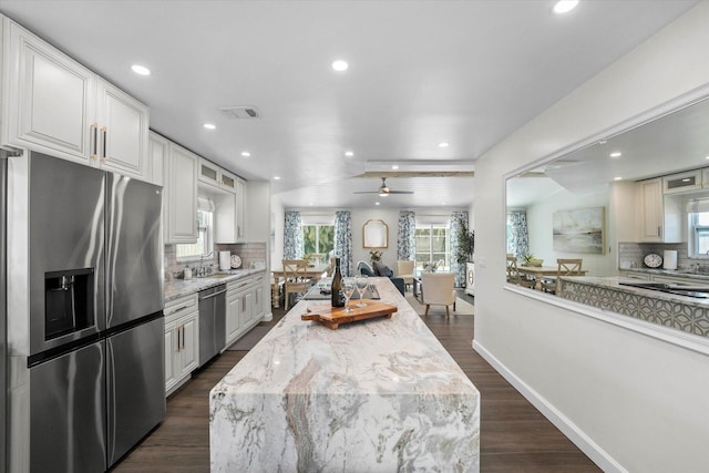 kitchen featuring appliances with stainless steel finishes, dark wood-type flooring, decorative backsplash, light stone counters, and ceiling fan