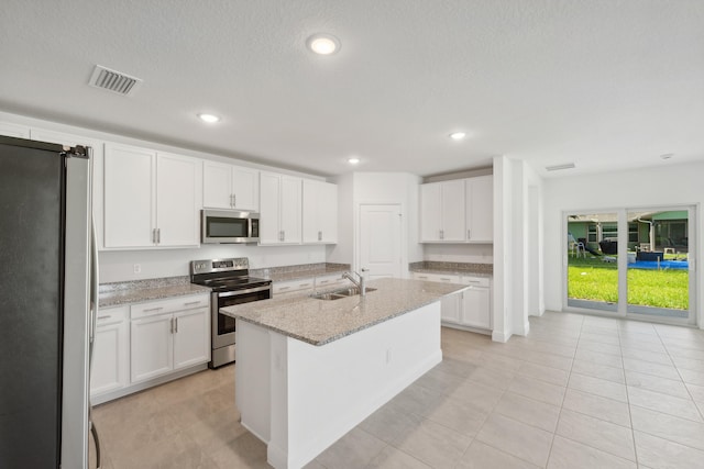 kitchen with white cabinetry, light stone counters, appliances with stainless steel finishes, and an island with sink