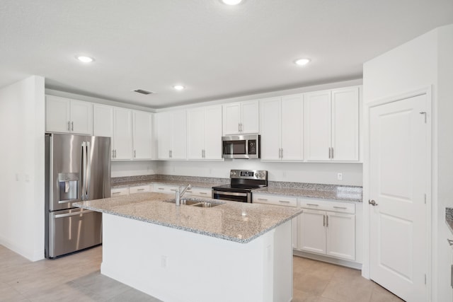 kitchen with appliances with stainless steel finishes, sink, an island with sink, white cabinets, and light stone counters