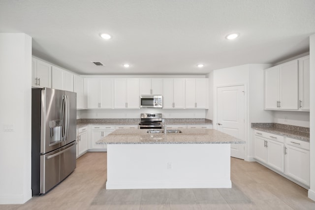 kitchen with light stone counters, appliances with stainless steel finishes, a center island with sink, and white cabinets