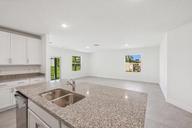 kitchen featuring stainless steel dishwasher, white cabinetry, light stone countertops, and sink