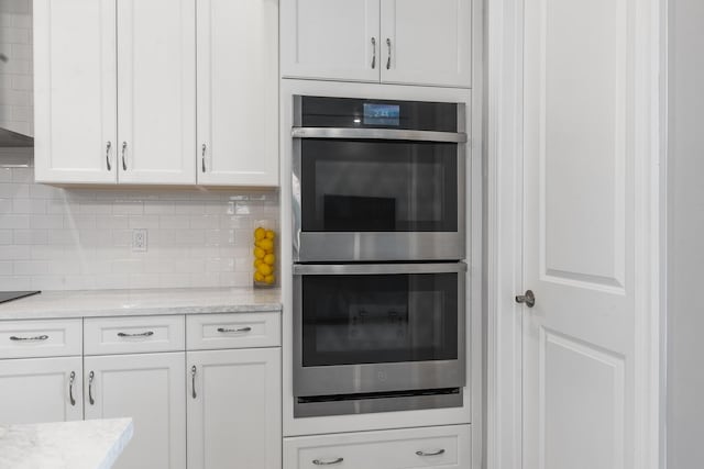 kitchen with double oven, backsplash, white cabinetry, and light stone countertops