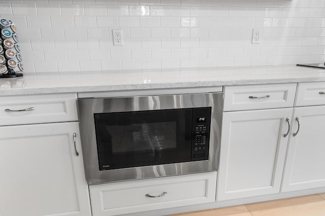 details with light stone countertops, backsplash, white cabinetry, and built in microwave