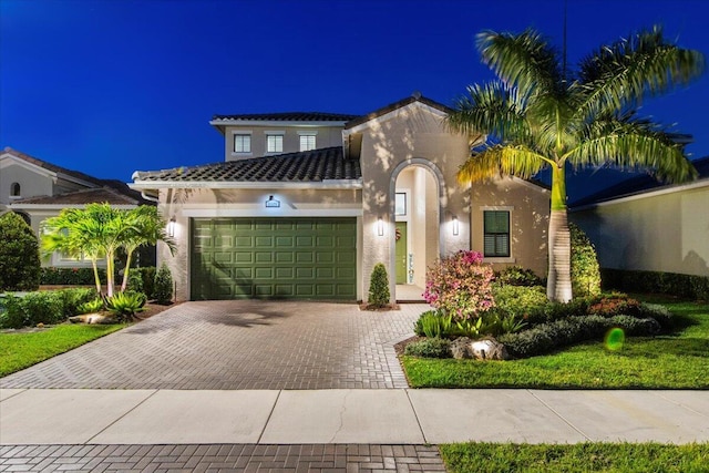 mediterranean / spanish-style house featuring decorative driveway, a tile roof, an attached garage, and stucco siding