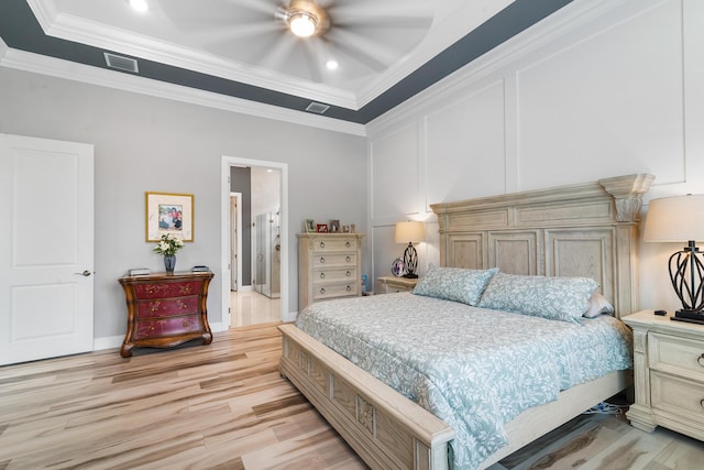 bedroom featuring light wood finished floors, visible vents, a decorative wall, and crown molding