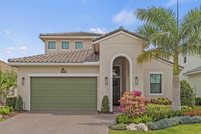 mediterranean / spanish-style home with decorative driveway, an attached garage, a tile roof, and stucco siding