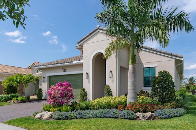 mediterranean / spanish-style house featuring a tiled roof, decorative driveway, an attached garage, and stucco siding