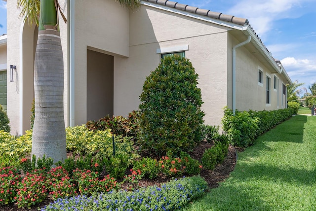 view of side of home with a yard, a tile roof, and stucco siding