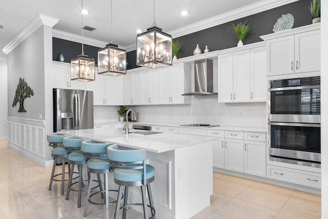 kitchen featuring a center island with sink, wall chimney exhaust hood, stainless steel appliances, ornamental molding, and a kitchen breakfast bar