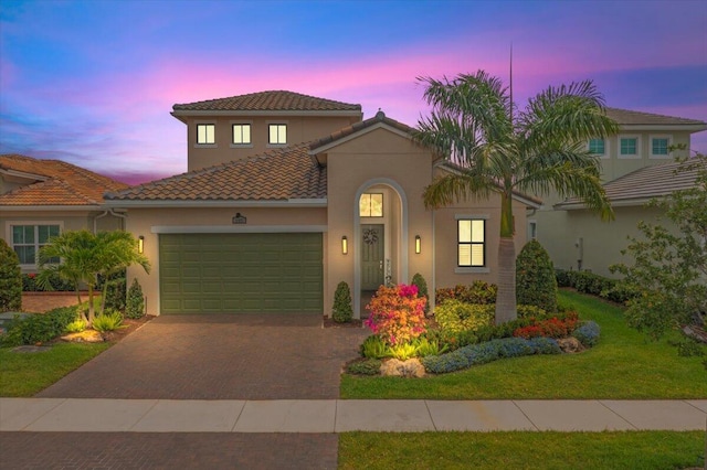 mediterranean / spanish-style house with decorative driveway, an attached garage, a tile roof, and stucco siding