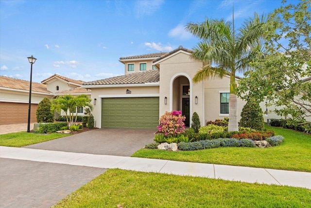 mediterranean / spanish home with an attached garage, a tiled roof, decorative driveway, stucco siding, and a front yard