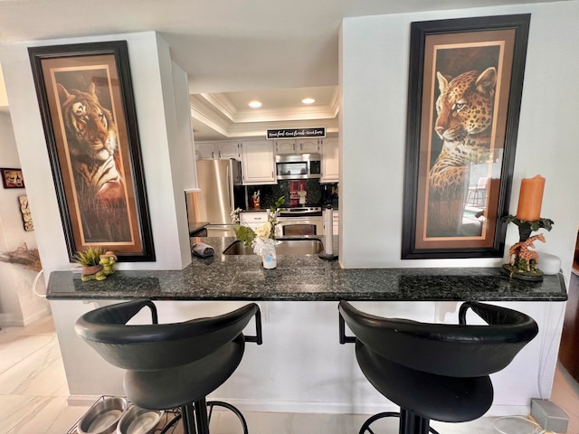 bar with dark stone countertops, tasteful backsplash, crown molding, a raised ceiling, and stainless steel appliances