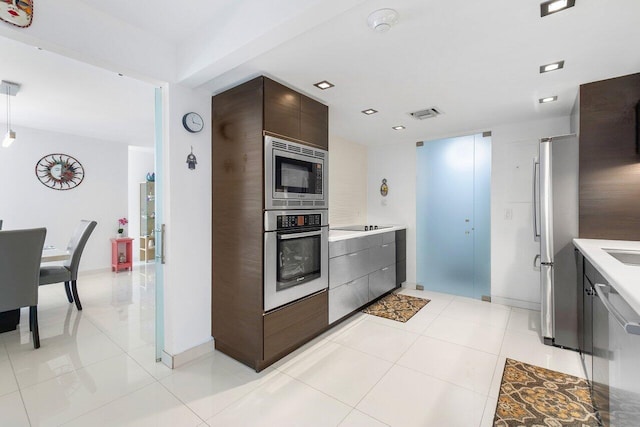 kitchen with appliances with stainless steel finishes, light tile patterned flooring, and dark brown cabinetry