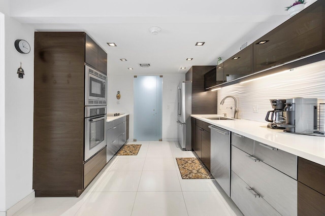 kitchen with light tile patterned floors, tasteful backsplash, appliances with stainless steel finishes, dark brown cabinets, and sink