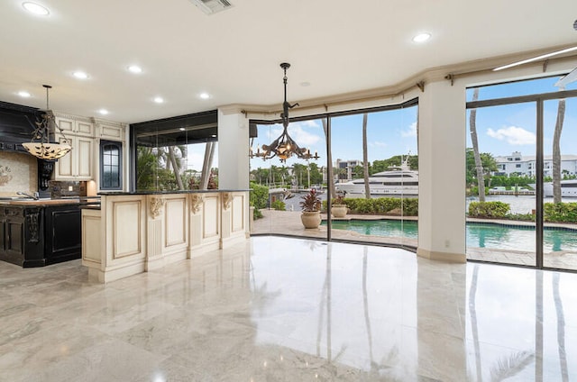 kitchen with cream cabinets, tasteful backsplash, a healthy amount of sunlight, and a notable chandelier