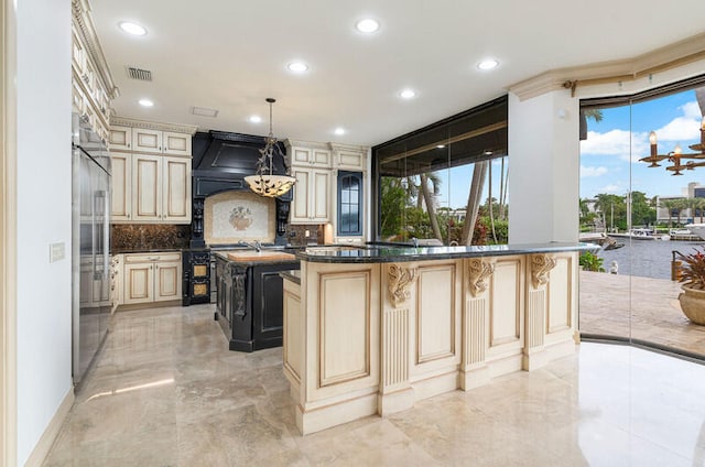 kitchen featuring a center island, hanging light fixtures, backsplash, cream cabinets, and custom exhaust hood