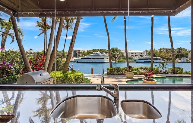 exterior space featuring grilling area, sink, a water view, and an outdoor kitchen