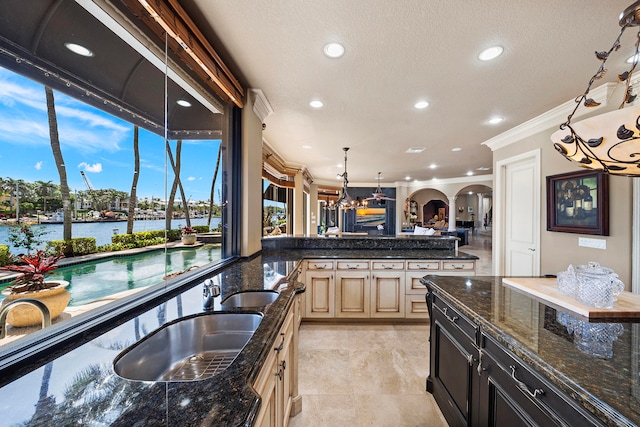 kitchen with pendant lighting, sink, ornamental molding, and dark stone countertops