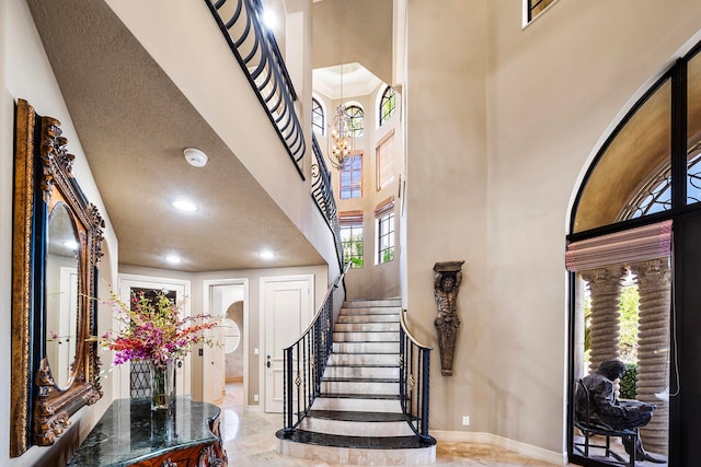 foyer entrance featuring a towering ceiling, a healthy amount of sunlight, a textured ceiling, and an inviting chandelier