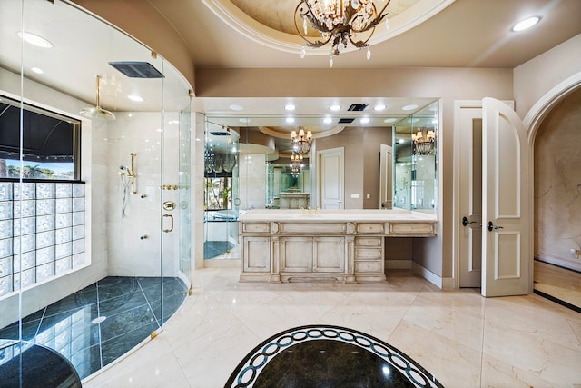 bathroom featuring a tray ceiling, vanity, a shower with shower door, and a notable chandelier