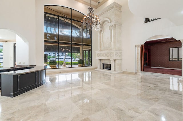 unfurnished living room featuring a premium fireplace, crown molding, a high ceiling, and a notable chandelier