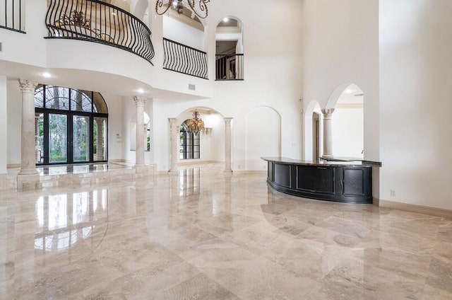 unfurnished living room featuring a high ceiling, decorative columns, an inviting chandelier, and french doors