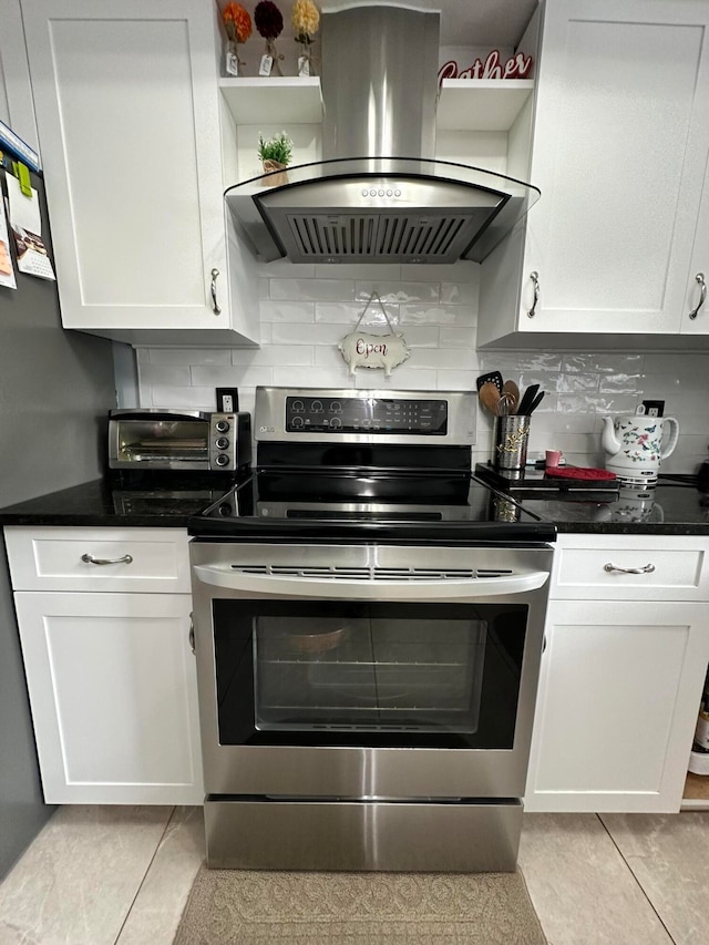 kitchen with island range hood, tasteful backsplash, light tile patterned flooring, electric range, and white cabinetry