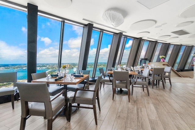 dining area featuring a wall of windows, a water view, and light hardwood / wood-style flooring