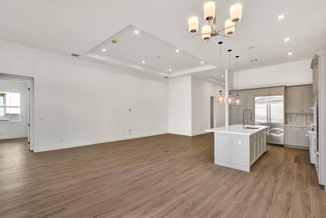 kitchen featuring sink, hanging light fixtures, a center island with sink, stainless steel appliances, and backsplash