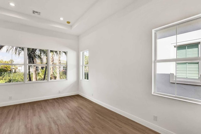spare room with a tray ceiling, recessed lighting, baseboards, visible vents, and wood finished floors
