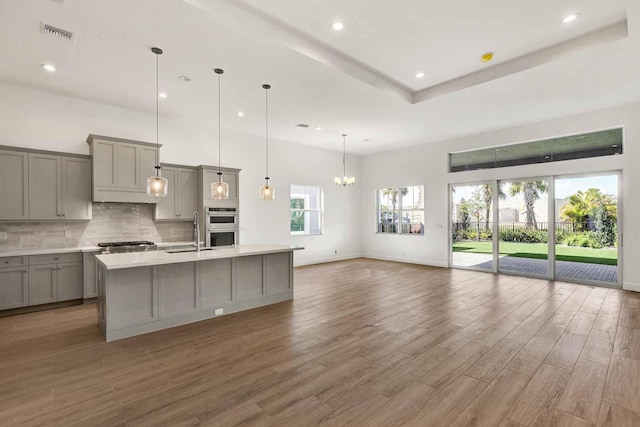 kitchen featuring sink, gray cabinets, a kitchen island with sink, backsplash, and decorative light fixtures