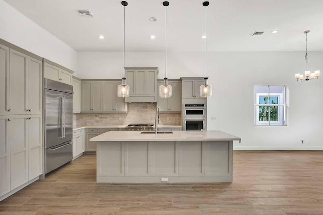 kitchen featuring decorative light fixtures, an island with sink, sink, gray cabinetry, and stainless steel appliances