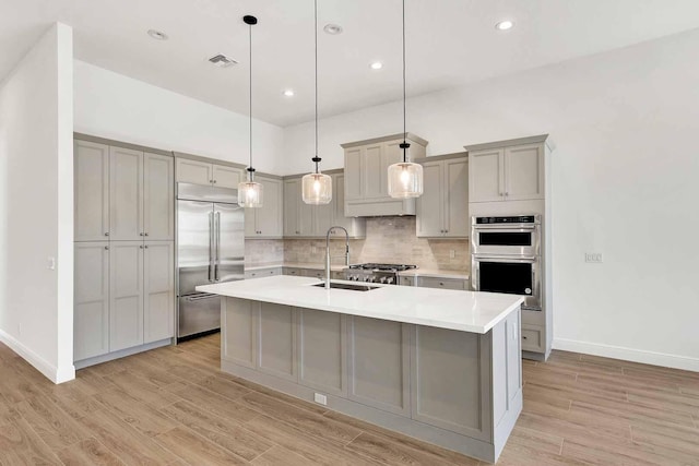 kitchen with pendant lighting, an island with sink, sink, gray cabinetry, and stainless steel appliances