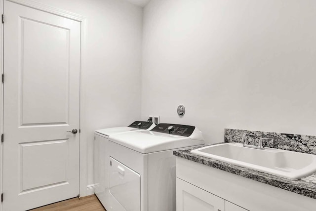 laundry room featuring cabinets, sink, washing machine and clothes dryer, and light hardwood / wood-style flooring