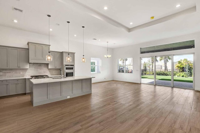 kitchen featuring gray cabinets, backsplash, a sink, wood finished floors, and visible vents