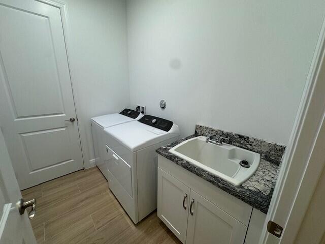 laundry area featuring washing machine and clothes dryer, cabinets, sink, and light hardwood / wood-style floors