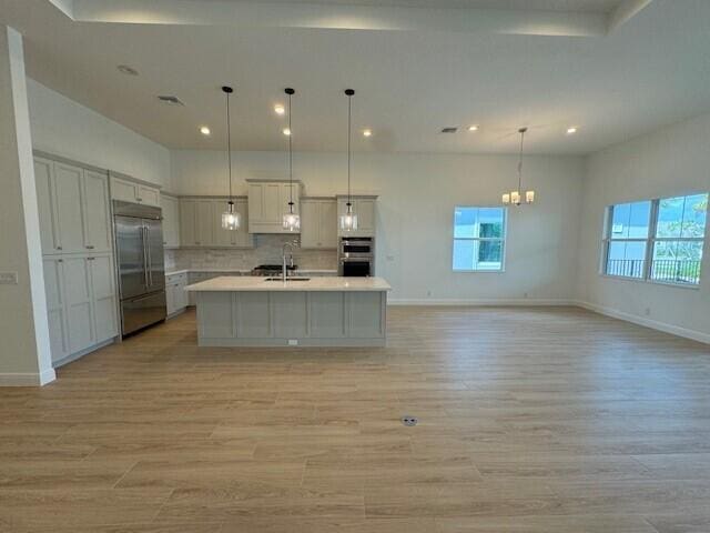 kitchen with hanging light fixtures, light hardwood / wood-style flooring, stainless steel appliances, sink, and a kitchen island with sink