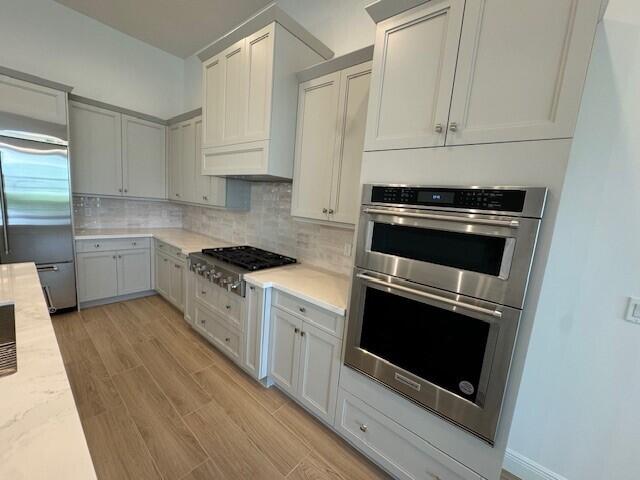 kitchen with light hardwood / wood-style flooring, light stone counters, appliances with stainless steel finishes, and decorative backsplash