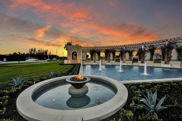 pool at dusk featuring pool water feature and a yard