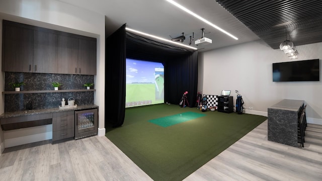 recreation room with baseboards, wine cooler, bar, light wood-type flooring, and golf simulator