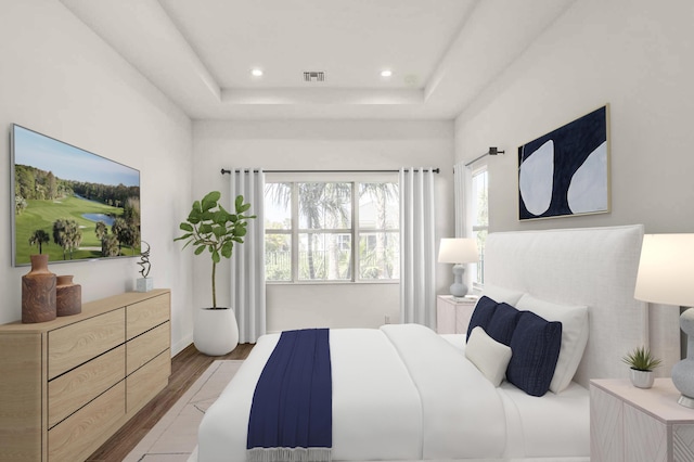 bedroom featuring multiple windows, visible vents, light wood-style floors, and a raised ceiling