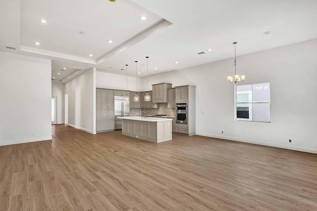 kitchen with appliances with stainless steel finishes, gray cabinetry, hanging light fixtures, light hardwood / wood-style floors, and a center island with sink