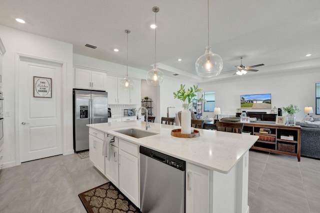 kitchen featuring ceiling fan, tasteful backsplash, stainless steel appliances, a center island with sink, and white cabinets