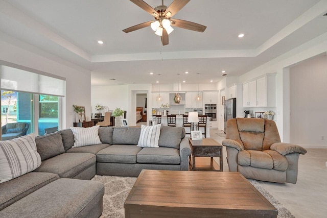 living room featuring light tile floors, ceiling fan, and a raised ceiling