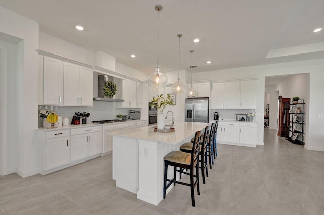 kitchen with appliances with stainless steel finishes, wall chimney range hood, a kitchen island with sink, and tasteful backsplash