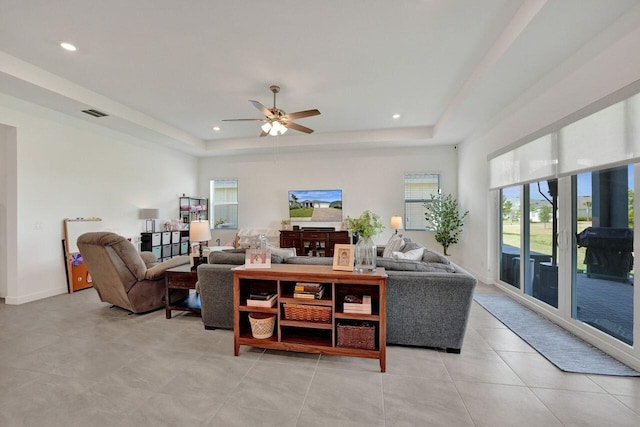 tiled living room with ceiling fan and a tray ceiling